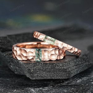 Könnte beinhalten: Zwei roségoldene Eheringe mit gehämmerter Textur. Jeder Ring ist mit einem grünen Edelstein besetzt.