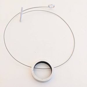 May include: A silver necklace with a circular pendant. The pendant is made of white metal with a black center and a thin silver wire running through it.