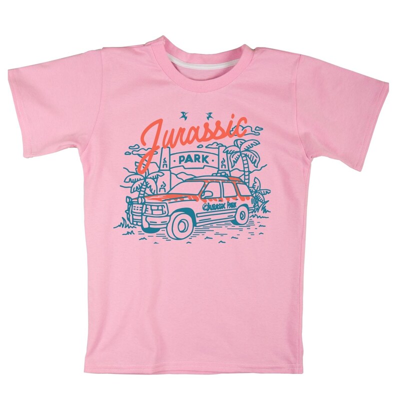 Pu&ograve; includere: Maglietta rosa con una grafica blu e arancione di una jeep che guida attraverso una giungla con il testo "Jurassic Park" sul lato della jeep.