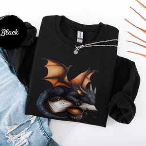 Cozy sweatshirt with cute black dragon sleeping on book on dragonkind with mug of coffee with moon phase pattern. Fourth wing Tairn Andarna dragons bookish booktok bookstagram  fantasy fan reader romantasy coffee lover gift idea soft warm sweater GOT