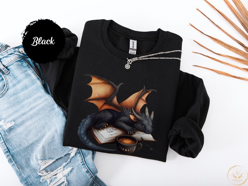 Cozy sweatshirt with cute black dragon sleeping on book on dragonkind with mug of coffee with moon phase pattern. Fourth wing Tairn Andarna dragons bookish booktok bookstagram  fantasy fan reader romantasy coffee lover gift idea soft warm sweater GOT