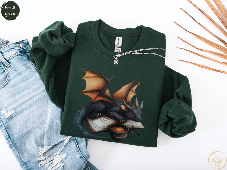 Cozy sweatshirt with cute black dragon sleeping on book on dragonkind with mug of coffee with moon phase pattern. Fourth wing Tairn Andarna dragons bookish booktok bookstagram  fantasy fan reader romantasy coffee lover gift idea soft warm sweater GOT