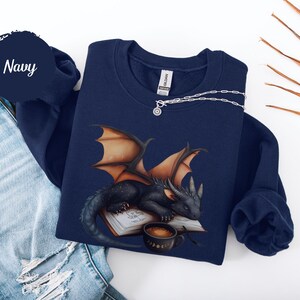 Cozy sweatshirt with cute black dragon sleeping on book on dragonkind with mug of coffee with moon phase pattern. Fourth wing Tairn Andarna dragons bookish booktok bookstagram  fantasy fan reader romantasy coffee lover gift idea soft warm sweater GOT