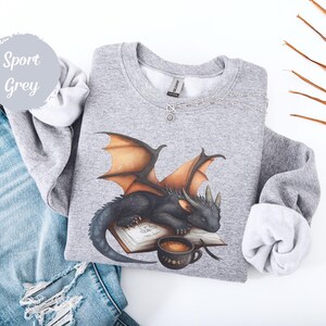 Cozy sweatshirt with cute black dragon sleeping on book on dragonkind with mug of coffee with moon phase pattern. Fourth wing Tairn Andarna dragons bookish booktok bookstagram  fantasy fan reader romantasy coffee lover gift idea soft warm sweater GOT