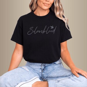 May include: Black crew neck t-shirt with the text "Silverblood" in a cursive font and a small bird graphic. The shirt is worn with light blue jeans. The word "Black" is in a black circle in the upper left corner.