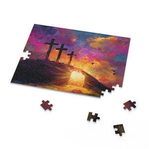 May include: A jigsaw puzzle depicting a sunset with three crosses on a hill. The sky blends from purple to orange, with a bright light shining from a cave. Several puzzle pieces are scattered around the partially assembled puzzle.