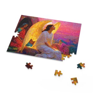 May include: A jigsaw puzzle depicting an angel with large, golden wings, seated and looking upwards. The artwork has a painterly style with vibrant colours, including pink, red, and yellow. Several puzzle pieces are scattered around the partially assembled puzzle.