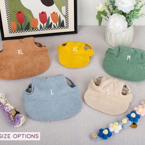 Pu&ograve; includere: Una collezione di cappelli per animali domestici in velluto a coste in vari colori, tra cui marrone, giallo e verde, ciascuno contrassegnato con una taglia: XL, XS e M. Sono inclusi anche cappelli blu e beige con taglie L e S. Sono inclusi anche due collari decorativi per animali domestici.