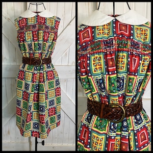 May include: A sleeveless vintage dress with a white collar and a colorful geometric pattern in red, green, yellow, and blue. The dress is cinched at the waist with a brown braided belt. The dress is displayed on a mannequin.