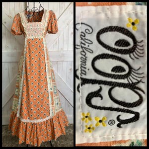Peut inclure: Une robe longue orange avec un motif floral répétitif bleu sarcelle et blanc, dotée de manches courtes bouffantes, d'une encolure carrée et d'une bordure en dentelle blanche. L'étiquette porte le texte "Ooh La California" avec des fleurs jaunes.