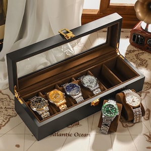May include: A black watch display case with a glass top, holding six wristwatches with various colored faces and metal bands. The case is open, revealing the watches on brown cushions. The background includes a world map and a vintage-style radio.