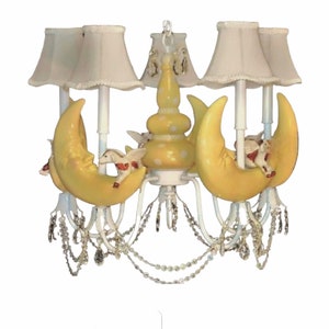May include: A white chandelier with yellow crescent moons and white horses. The chandelier has crystal-like beads hanging from it.