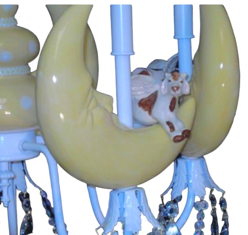 K&ouml;nnte beinhalten: Ein wei&szlig;er und gelber Keramik-Kronleuchter mit einem Halbmond-Design und einer kleinen Kuhfigur. Der Kronleuchter hat Kristall-Akzente und ist perfekt f&uuml;r ein Kinderzimmer oder ein Kinderzimmer.