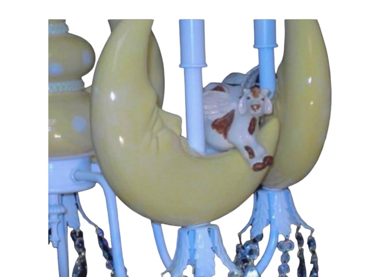 May include: A white and yellow ceramic chandelier with a crescent moon design and a small cow figurine sitting on top. The chandelier has crystal-like beads hanging from the bottom.