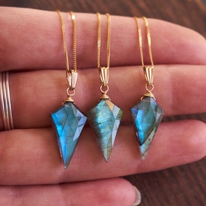 May include: Three gold necklaces with blue labradorite gemstone pendants in the shape of a teardrop. The pendants are faceted and have a shimmery, iridescent finish.