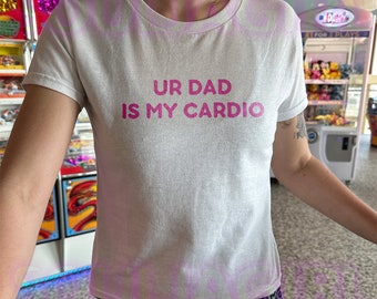 May include: White t-shirt with pink text that reads "UR DAD IS MY CARDIO"