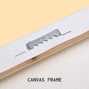 May include: Close-up of the back of a canvas frame, showing a metal sawtooth hanger and staples. The canvas is stretched over a wooden frame. Text at the bottom reads "CANVAS FRAME".