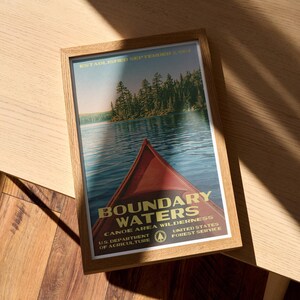 Peut inclure: Une affiche encadr&eacute;e montrant un cano&euml; rouge sur une eau bleue avec une for&ecirc;t en arri&egrave;re-plan. Le texte indique : ESTABLISHED SEPTEMBER 3, 1964, BOUNDARY WATERS CANOE AREA WILDERNESS, U.S. DEPARTMENT OF AGRICULTURE, UNITED STATES FOREST SERVICE.
