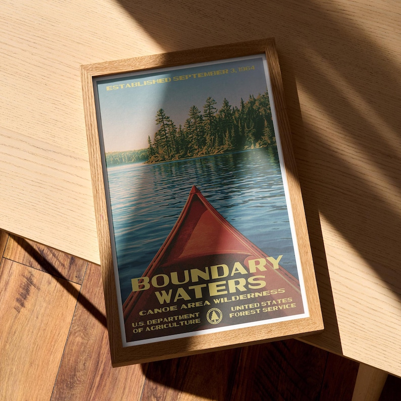 Peut inclure: Une affiche encadr&eacute;e montrant un cano&euml; rouge sur une eau bleue avec une for&ecirc;t en arri&egrave;re-plan. Le texte indique : ESTABLISHED SEPTEMBER 3, 1964, BOUNDARY WATERS CANOE AREA WILDERNESS, U.S. DEPARTMENT OF AGRICULTURE, UNITED STATES FOREST SERVICE.