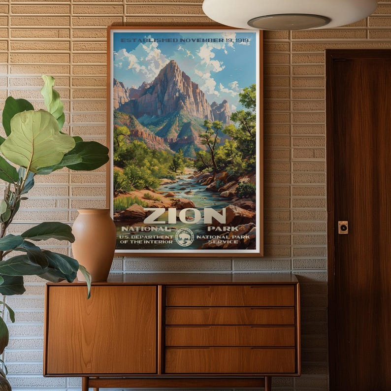 May include: A framed vintage poster of Zion National Park, featuring a mountain landscape with a river. The poster includes the text "ZION NATIONAL PARK" and "ESTABLISHED NOVEMBER 19, 1919". The poster is displayed on a wooden cabinet.