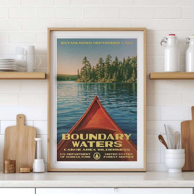 Peut inclure: Une affiche encadr&eacute;e montrant un cano&euml; rouge sur une eau bleue avec une for&ecirc;t en arri&egrave;re-plan. Le texte indique : ESTABLISHED SEPTEMBER 3, 1964, BOUNDARY WATERS CANOE AREA WILDERNESS, U.S. DEPARTMENT OF AGRICULTURE, UNITED STATES FOREST SERVICE.
