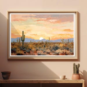Può includere: Una stampa paesaggistica incorniciata che raffigura una scena desertica al tramonto. L'opera presenta un sole luminoso basso all'orizzonte, montagne in silhouette e vari cactus sparsi su un primo piano di sterpaglie secche e strutturate.