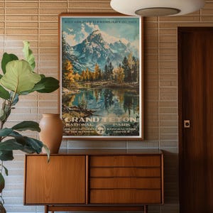 Pode incluir: Um cartaz vintage anunciando o Parque Nacional Grand Teton. O cartaz apresenta uma paisagem montanhosa c&ecirc;nica com um lago que reflete as montanhas. O texto do cartaz diz "Estabelecido em 26 de fevereiro de 1920" e "Grand Teton National Park".