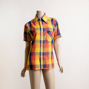 May include: A short-sleeved button-down shirt with a checkered pattern in shades of orange, yellow, blue, and brown. The shirt has a pointed collar and a single chest pocket.