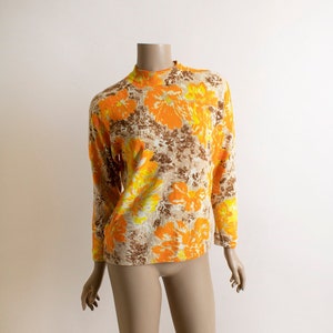 May include: A long-sleeved, mock neck sweater with a floral print in shades of orange, yellow, and brown.