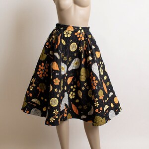 May include: A black midi skirt with a floral print featuring orange, yellow, and white flowers and leaves. The skirt is full and has a gathered waist.