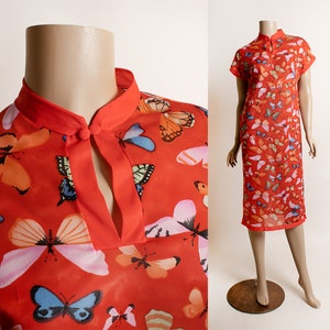 May include: A red, short-sleeved dress with a mandarin collar and a keyhole opening at the neckline. The dress is covered in a colorful butterfly print.
