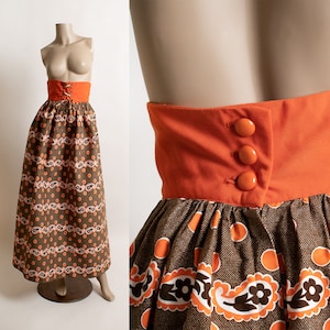 May include: A brown and orange patterned maxi skirt with a solid orange waistband and three orange buttons. The skirt has a fitted waist and a flowing, full skirt.