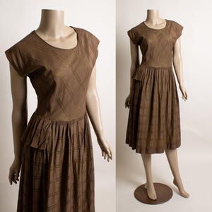 May include: Brown vintage dress with a plaid pattern. The dress features short sleeves, a round neckline, and a pleated skirt. The dress is displayed on a mannequin.