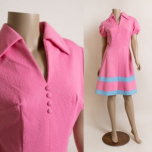 May include: A pink mini dress with a blue trim around the bottom. The dress has a collared neckline and short sleeves.