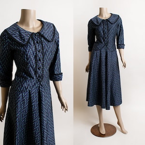 May include: A vintage dress with a black and white floral pattern. The dress has a large, white collar with black trim and a button-up front. The dress is fitted at the waist and has a full skirt.