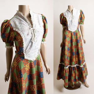May include: A floor-length dress featuring a patchwork pattern of green, blue, yellow, and orange squares. The bodice has a white eyelet fabric overlay with a lace-trimmed V-neckline and a tie closure. The sleeves are puffed with lace trim.