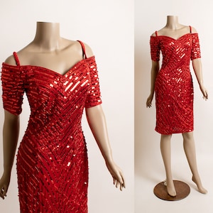 May include: A red sequined dress with a sweetheart neckline and off-the-shoulder straps. The dress has a fitted silhouette and a short length.