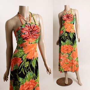 May include: A halter-neck maxi dress with a vibrant floral print. The dress features a black background with large orange flowers and green leaves. The bodice is embellished with a large, beaded flower. The dress is displayed on a mannequin.