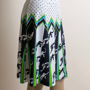 May include: A white skirt with a black and green geometric pattern and white polka dots. The skirt has a blue waistband.