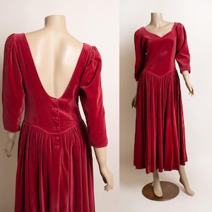 May include: A long, red velvet dress with a low back and a button closure. The dress has a fitted bodice and a full skirt.