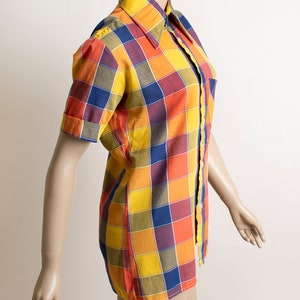 May include: A short-sleeved button-up shirt with a large plaid pattern in shades of yellow, orange, red, blue, and green.