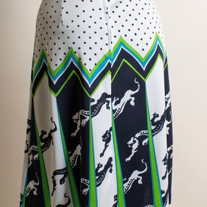 May include: A white skirt with a black and green geometric pattern and black animal silhouettes. The skirt has a zipper and button closure in the back.