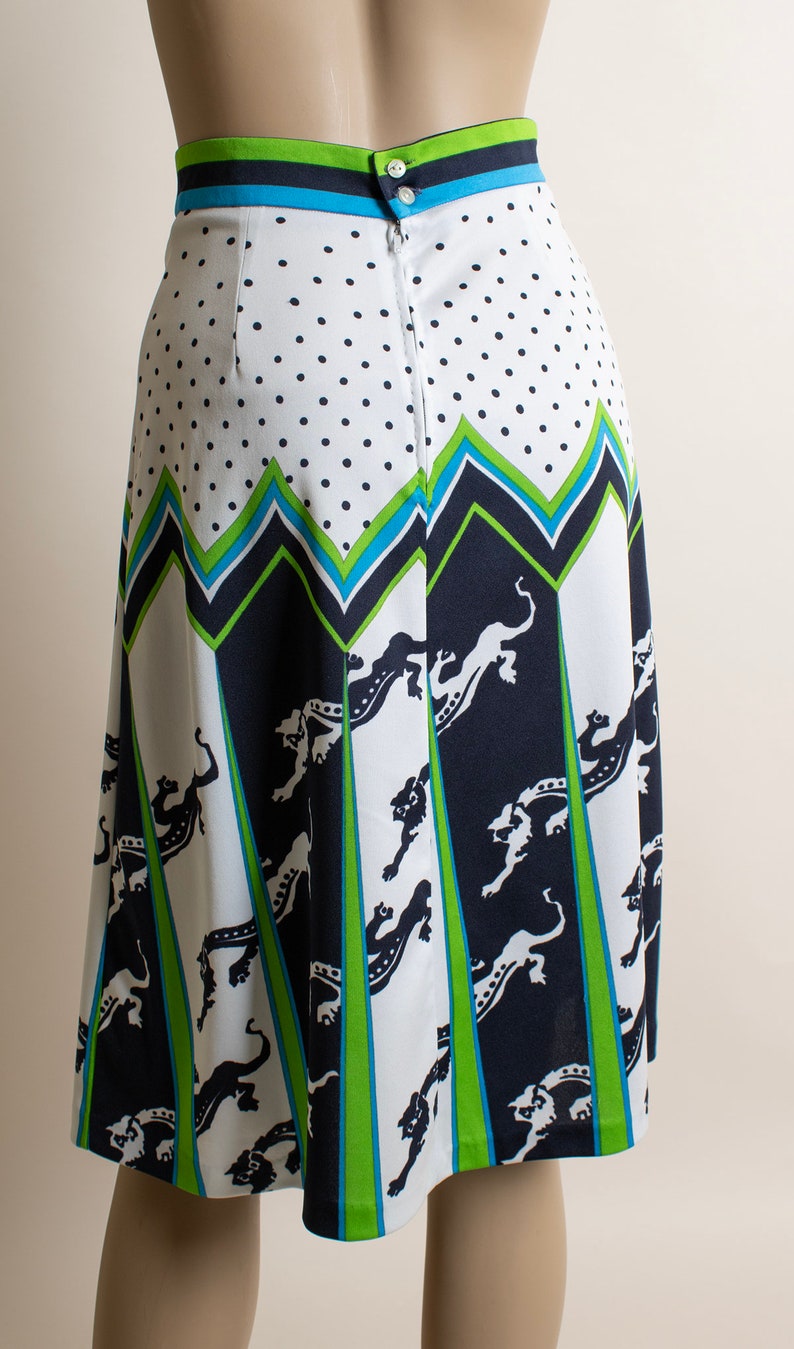 May include: A white skirt with a black and green geometric pattern and black animal silhouettes. The skirt has a zipper and button closure in the back.