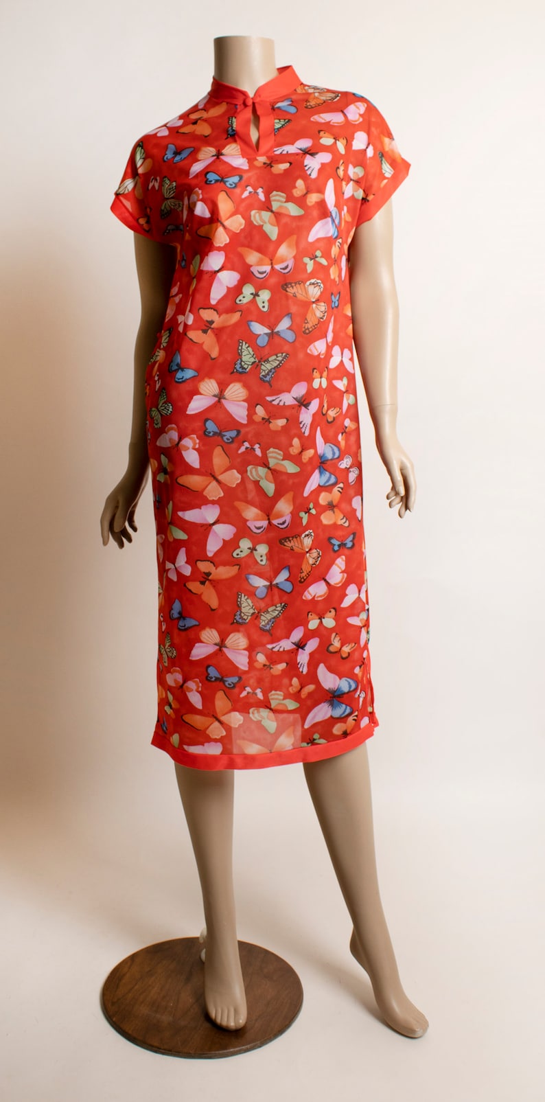 May include: A red dress with a mandarin collar and short sleeves. The dress is covered in a butterfly print with various colors, including pink, blue, and green.