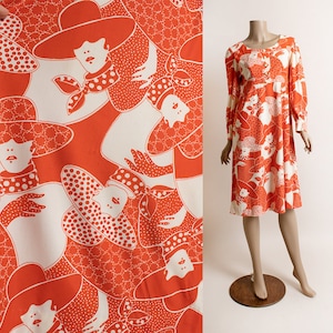May include: A vintage knee-length dress on a mannequin, featuring a repeating pattern of women in hats in white and orange. The dress has long sleeves and a scoop neckline. The fabric is displayed on the left, showing the pattern up close.