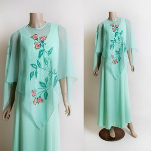 May include: A mint green maxi dress with a sheer overlay featuring a floral design with pink roses and green leaves. The dress has a long, flowing skirt and a fitted bodice.