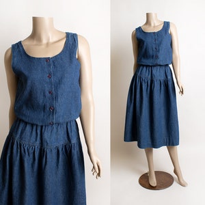 May include: A sleeveless denim dress with a button-up bodice and a tiered skirt. The dress is a dark blue color and has a relaxed fit.