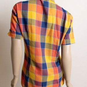 May include: A short-sleeved button-down shirt with a checkered pattern in shades of yellow, orange, blue, and purple.