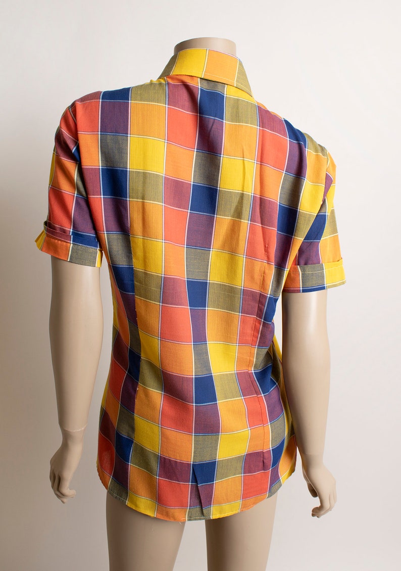 May include: A short-sleeved button-down shirt with a checkered pattern in shades of yellow, orange, blue, and purple.