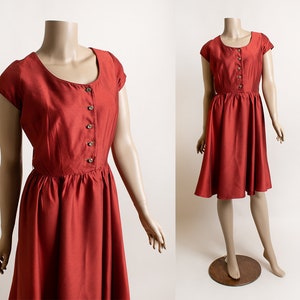 May include: A red vintage dress with a button-up front and short sleeves. The dress has a fitted bodice and a full skirt.